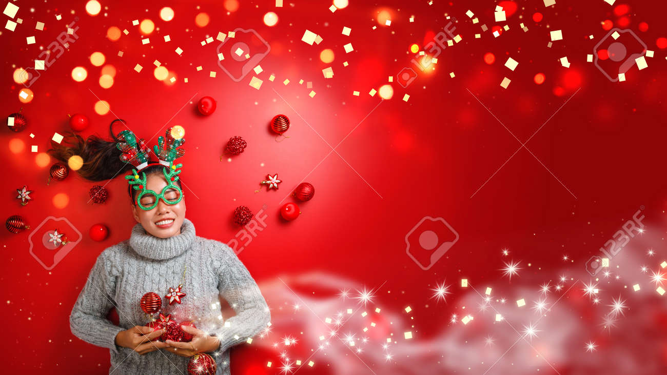 Christmas New Year. Young Woman dressed in warm sweater with Props ball red with christmas ornaments in Holiday on shine red background. Concept merry christmas. - 160113319 Christmas New Year. Young Woman dressed in warm sweater with Props ball red with christmas ornaments in Holiday on shine red background. Concept merry christmas. - 160113319