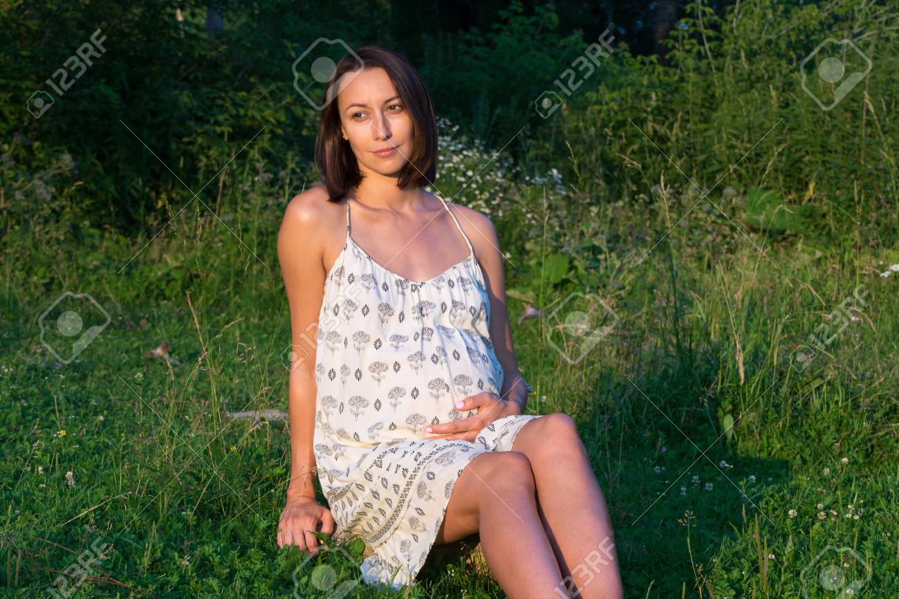 草の上に座って妊娠中の女の子は 胃の日当たりの良い夏の夜自身を保持します の写真素材 画像素材 Image