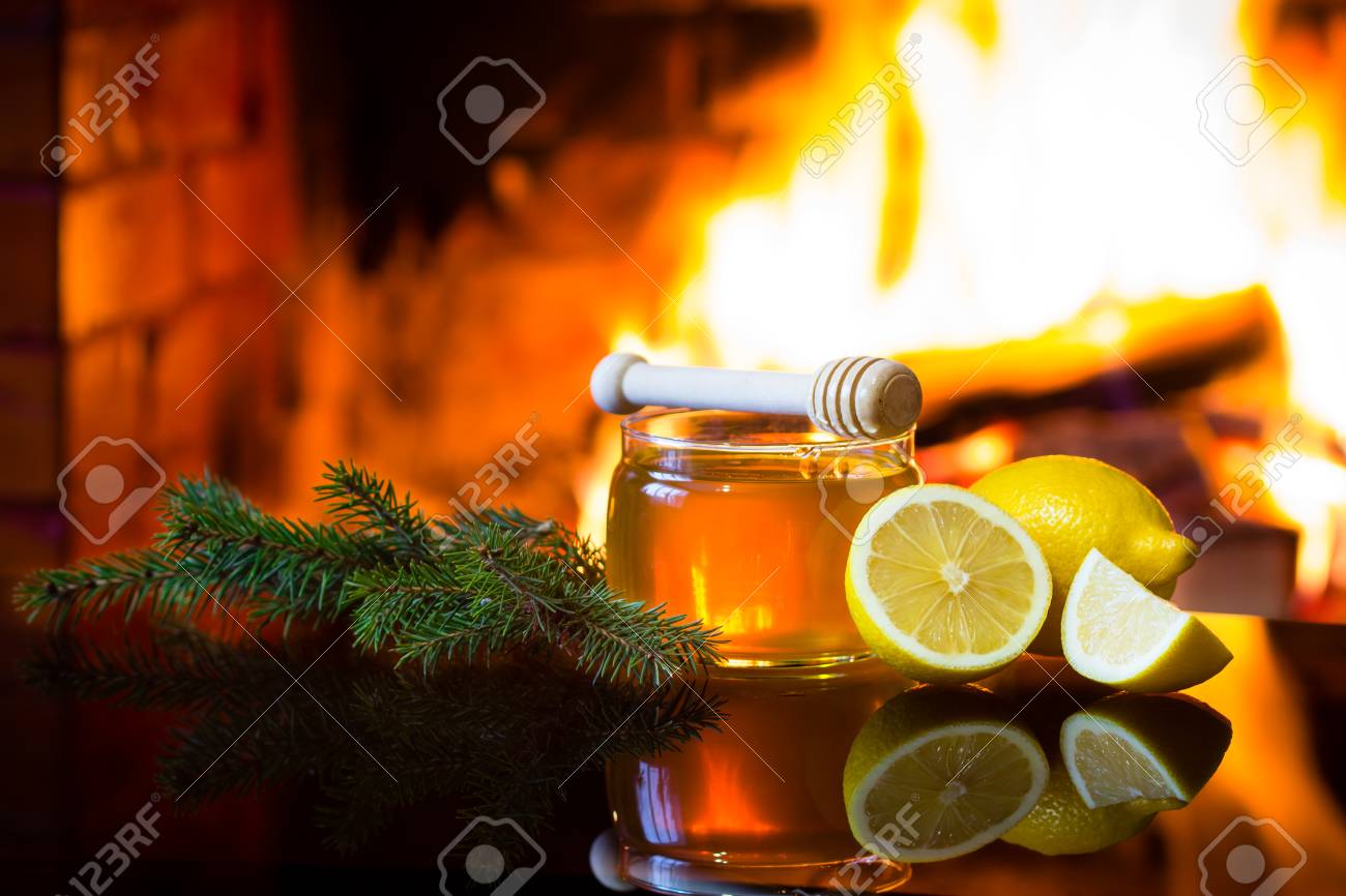Christmas New Year composition. Jar of bee honey, lemon with christmas decoration - fir branches in front of warm fireplace. Relaxed, magical, cozy atmosphere near fireplace - 64888197 Christmas New Year composition. Jar of bee honey, lemon with christmas decoration - fir branches in front of warm fireplace. Relaxed, magical, cozy atmosphere near fireplace - 64888197