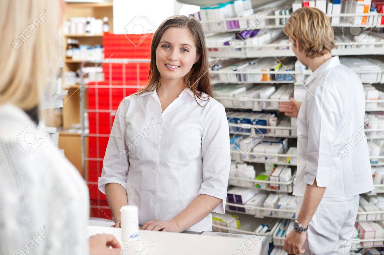 Pharmacist smiling while attending customer at counter - 12766930 Pharmacist smiling while attending customer at counter - 12766930