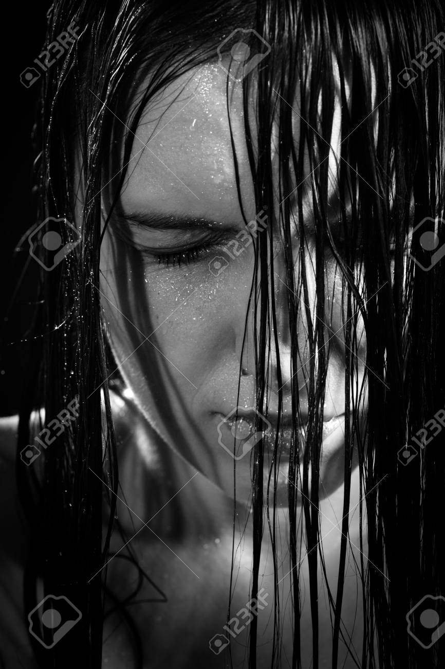 Serious sad woman with wet black hair close her eyes in dark monochrome stock photo