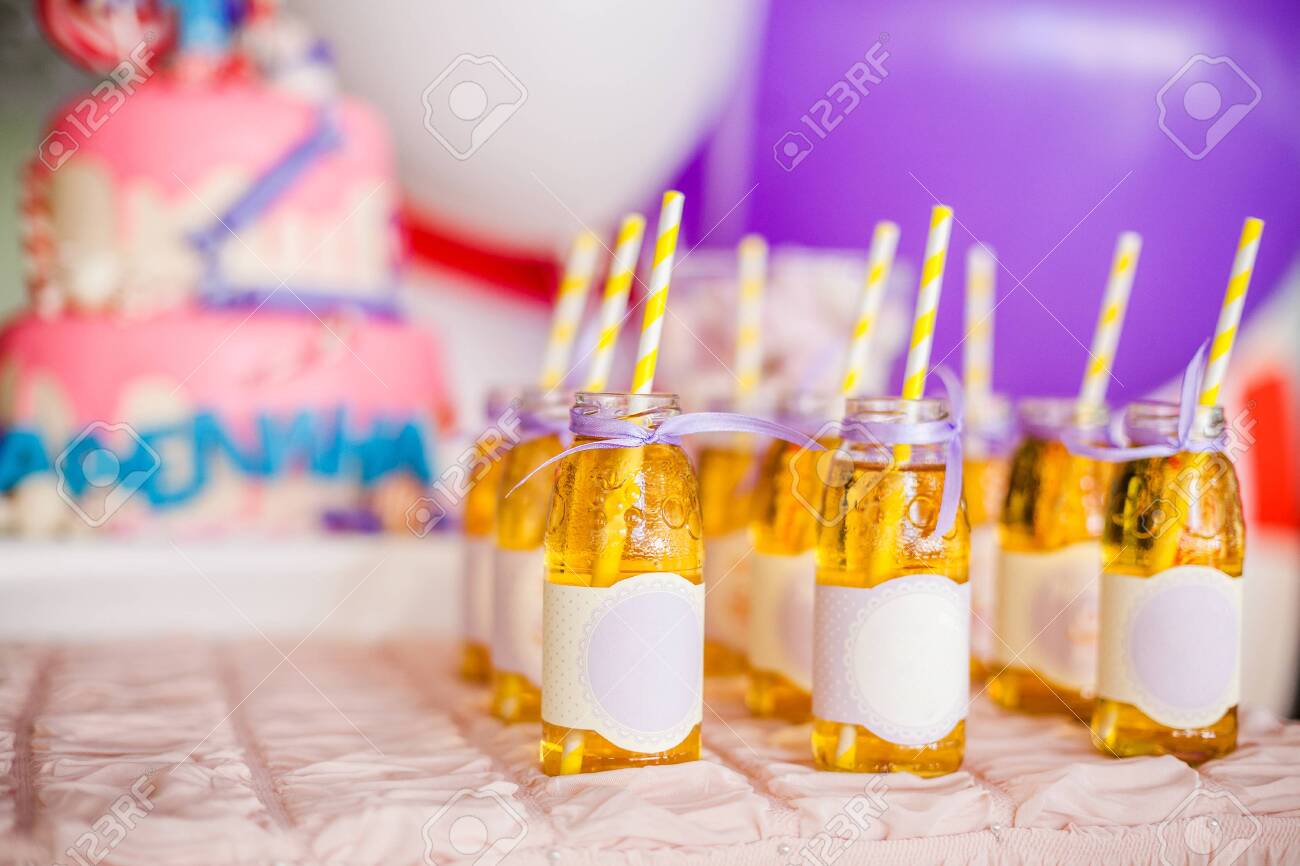 Birthday party concept, candy bar for children. A lot of bottles of apple juice, white and yellow straws, big pink cake and white and purple ballons on background - 120314760 Birthday party concept, candy bar for children. A lot of bottles of apple juice, white and yellow straws, big pink cake and white and purple ballons on background - 120314760