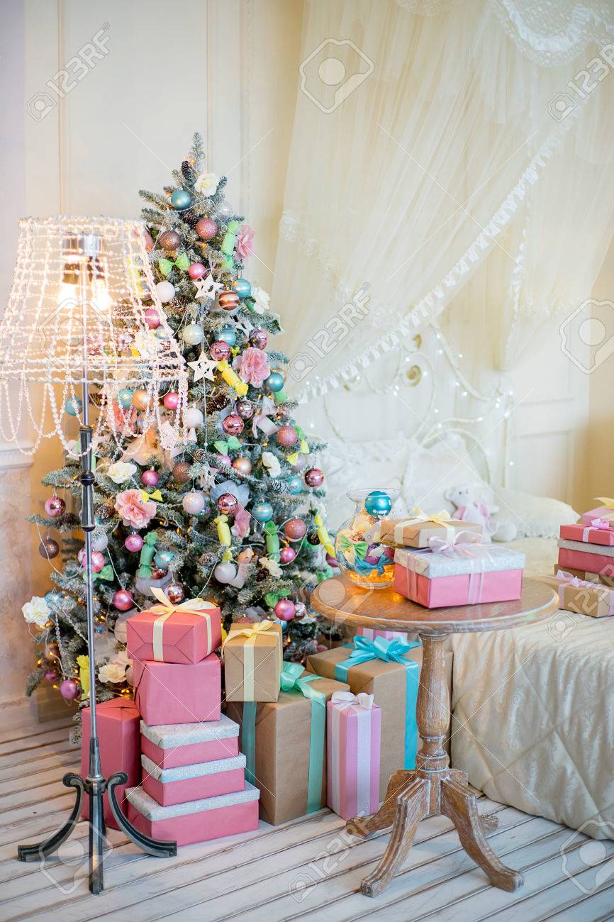 ベッド 床ランプ 錬鉄の椅子およびテーブルの横にあるギフトとクリスマス ツリー パステル カラーのクリスマス インテリア の写真素材 画像素材 Image