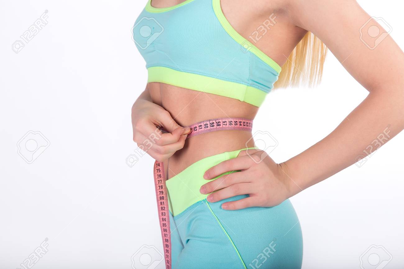 Weight loss, slim body, healthy lifestyle concept. Fitness girl measuring her waistline with measure tape on white background. - 77959150 Weight loss, slim body, healthy lifestyle concept. Fitness girl measuring her waistline with measure tape on white background. - 77959150