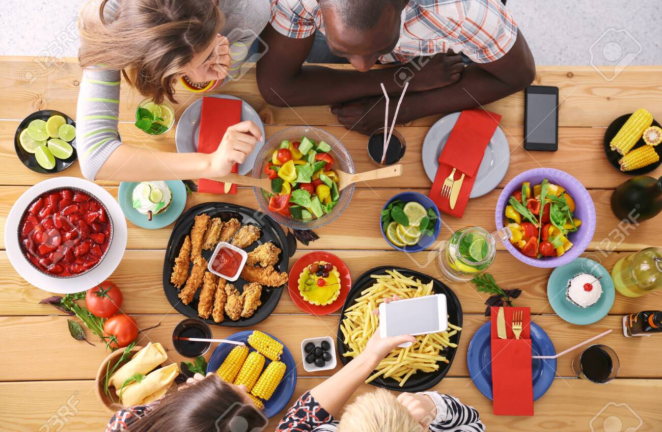 Top view of group of people having dinner together while sitting at wooden table. Food on the table. People eat fast food. - 129463705 Top view of group of people having dinner together while sitting at wooden table. Food on the table. People eat fast food. - 129463705