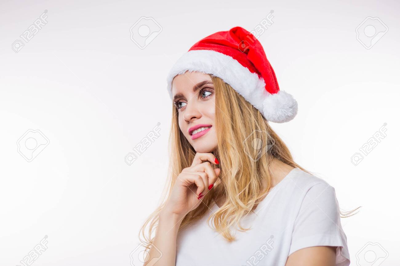 Happy charming blonde woman in red Santa hat and t-shirt looking with smile to the side on white background with copy space. Christmas, new year and celebration concept - 134834992 Happy charming blonde woman in red Santa hat and t-shirt looking with smile to the side on white background with copy space. Christmas, new year and celebration concept - 134834992