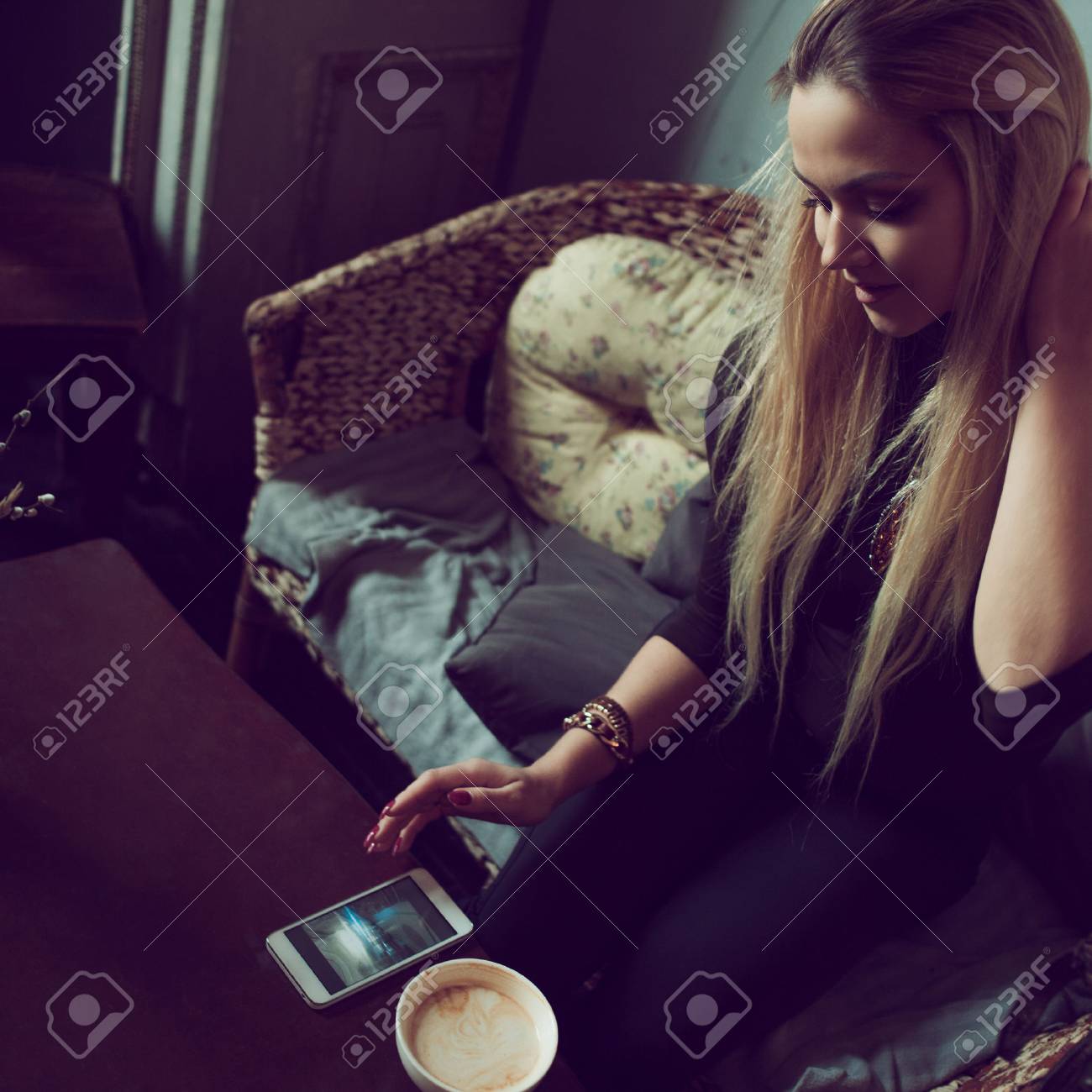 若い魅力的な女性フリーランサーはビンテージ カフェのソファに座りながら携帯電話でおしゃべり 快適なコーヒー ショップでの作業中にテキスト メッセージを読む朝のコーヒーを飲む の写真素材 画像素材 Image