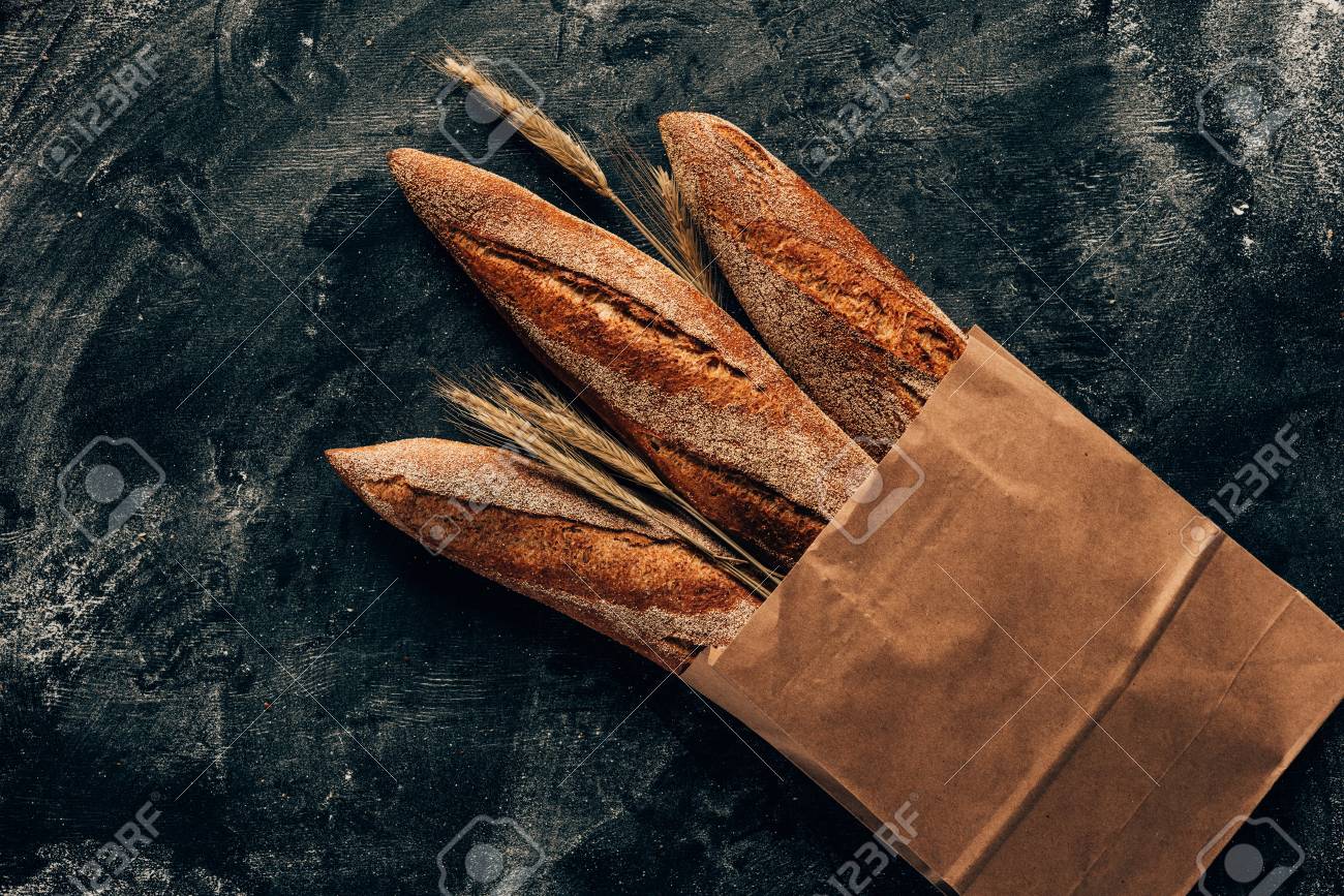 top view of arranged french baguettes in paper bag and wheat on dark tabletop with flour - 97453430 top view of arranged french baguettes in paper bag and wheat on dark tabletop with flour - 97453430