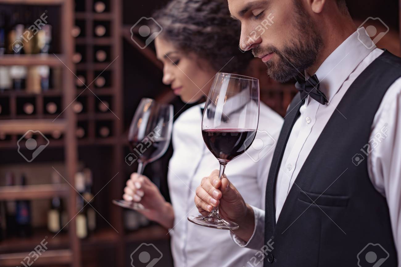 Two sommeliers, male and female tasting red wine in cellar - 102353938 Two sommeliers, male and female tasting red wine in cellar - 102353938