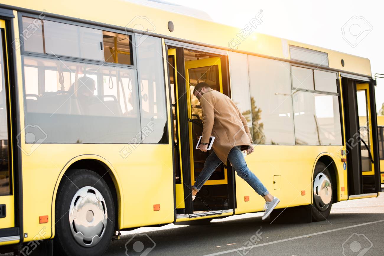 full length view of young man holding digital tablet and entering bus - 102323215 full length view of young man holding digital tablet and entering bus - 102323215