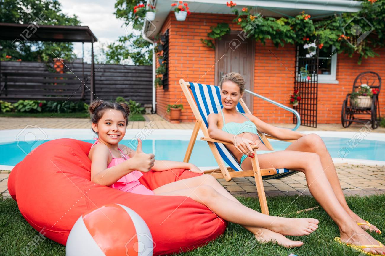 mother and smiling daughter resting near swimming pool on backyard on summer day - 106105221 mother and smiling daughter resting near swimming pool on backyard on summer day - 106105221