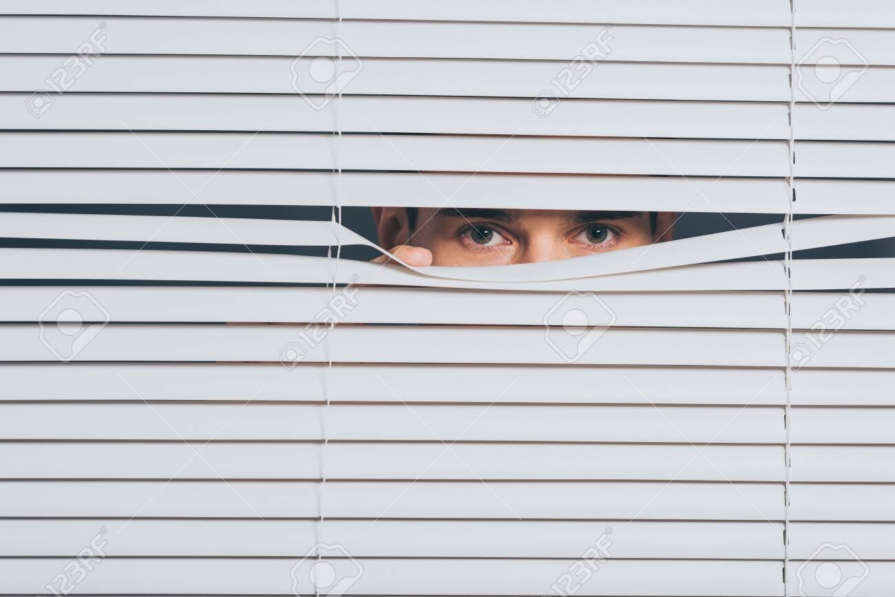 Suspicious Young Man Peeking And Looking At Camera Through Blinds ...
