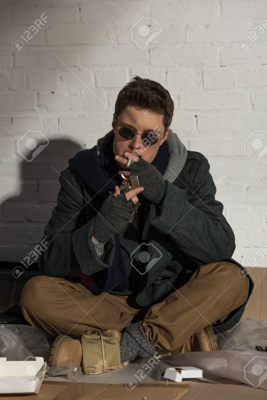 Homeless Man Lighting Cigarette While Sitting By Brick Wall Stock Photo,  Picture and Royalty Free Image. Image 117877611