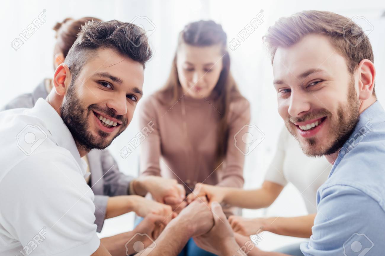 group of people sitting, smiling and stacking hands during therapy session - 120077033 group of people sitting, smiling and stacking hands during therapy session - 120077033