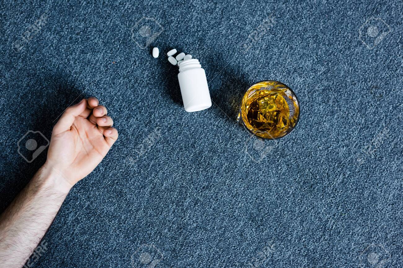 Cropped view of man lying on grey floor near glass of whiskey and container with pills - 123533457 Cropped view of man lying on grey floor near glass of whiskey and container with pills - 123533457