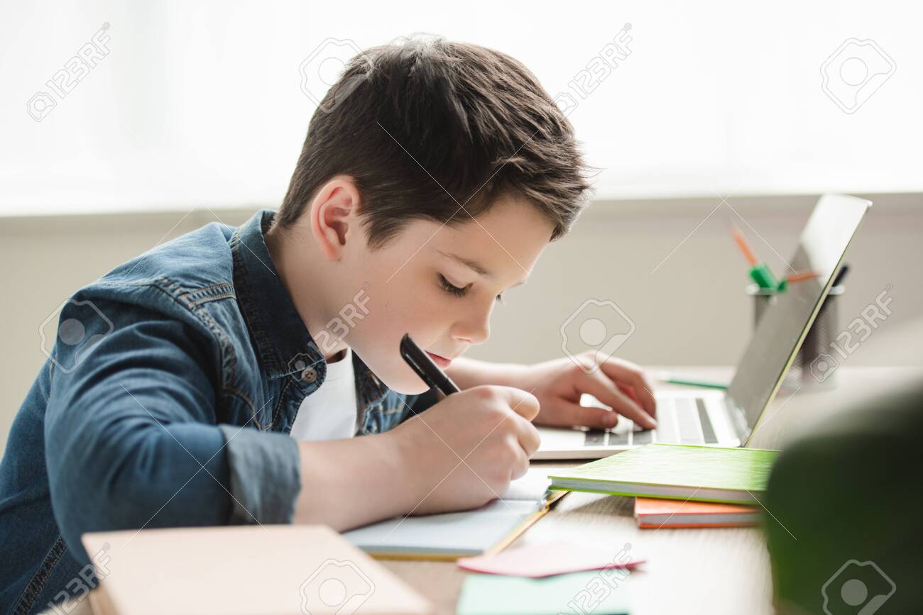 adorable attentive boy writing in notebook and using laptop while doing homework - 123661640 adorable attentive boy writing in notebook and using laptop while doing homework - 123661640