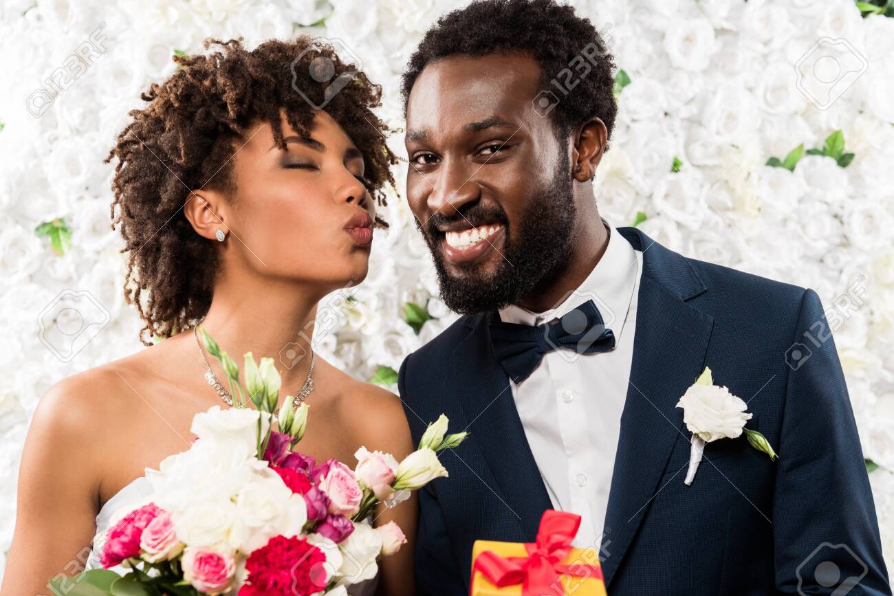 african american bride with duck face holding bouquet with flowers near cheerful bridegroom - 128144418 african american bride with duck face holding bouquet with flowers near cheerful bridegroom - 128144418