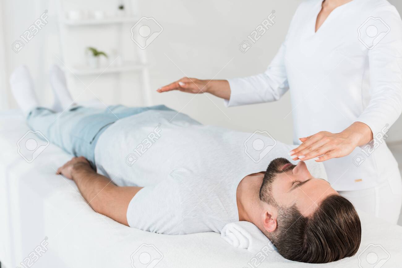 cropped view of healer with hands above body of man resting on massage table - 128146990 cropped view of healer with hands above body of man resting on massage table - 128146990