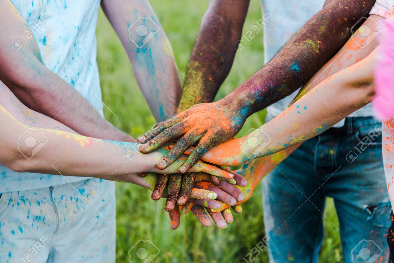 cropped view of multicultural friends with colorful holi paints putting hands together - 128186026 cropped view of multicultural friends with colorful holi paints putting hands together - 128186026