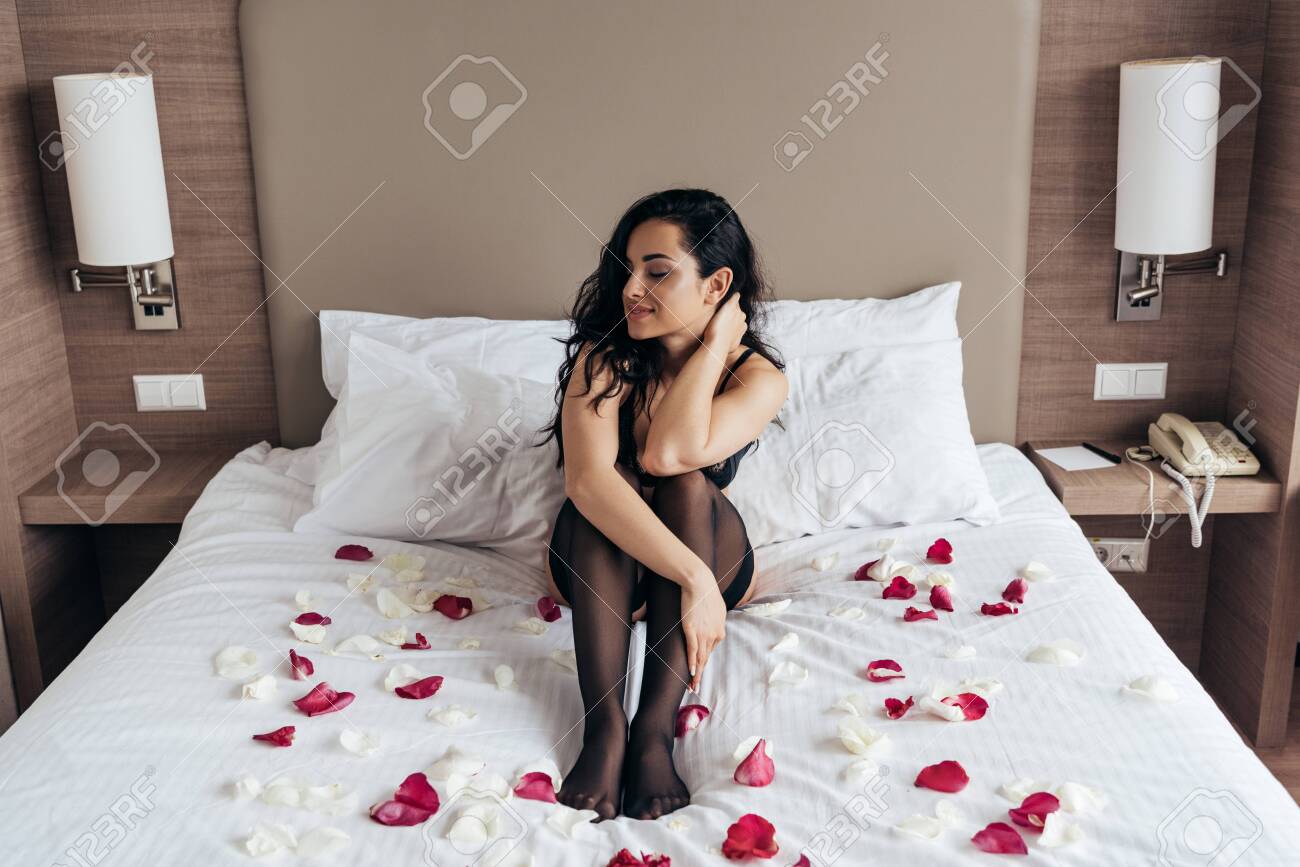 brunette girl in black stockings sitting on bed with rose petals in bedroom - 128157757 brunette girl in black stockings sitting on bed with rose petals in bedroom - 128157757