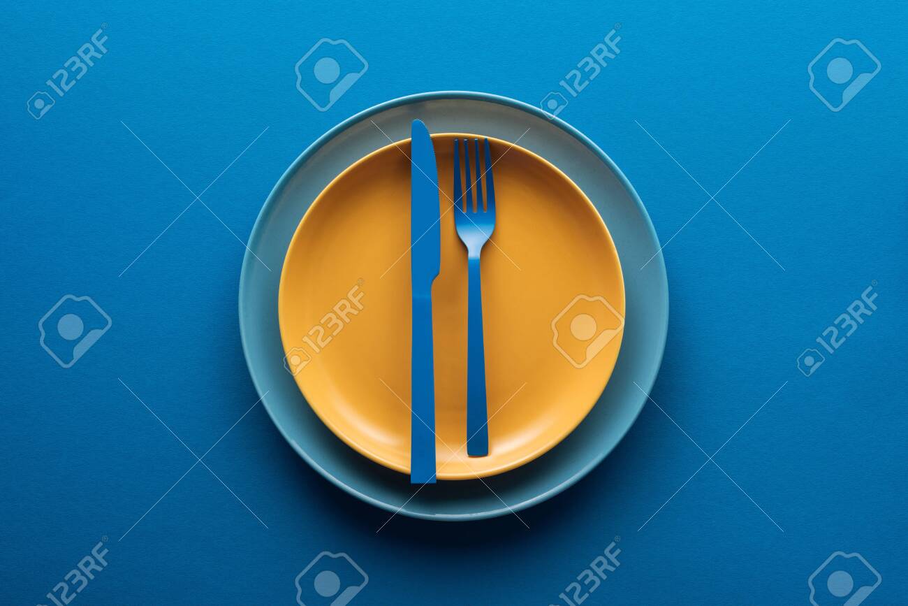 top view of blue plastic knife and fork on yellow plate above another plate on blue background - 130305228 top view of blue plastic knife and fork on yellow plate above another plate on blue background - 130305228