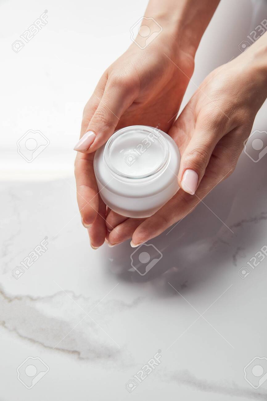 cropped view of woman holding jar with cream on white surface - 130498946 cropped view of woman holding jar with cream on white surface - 130498946