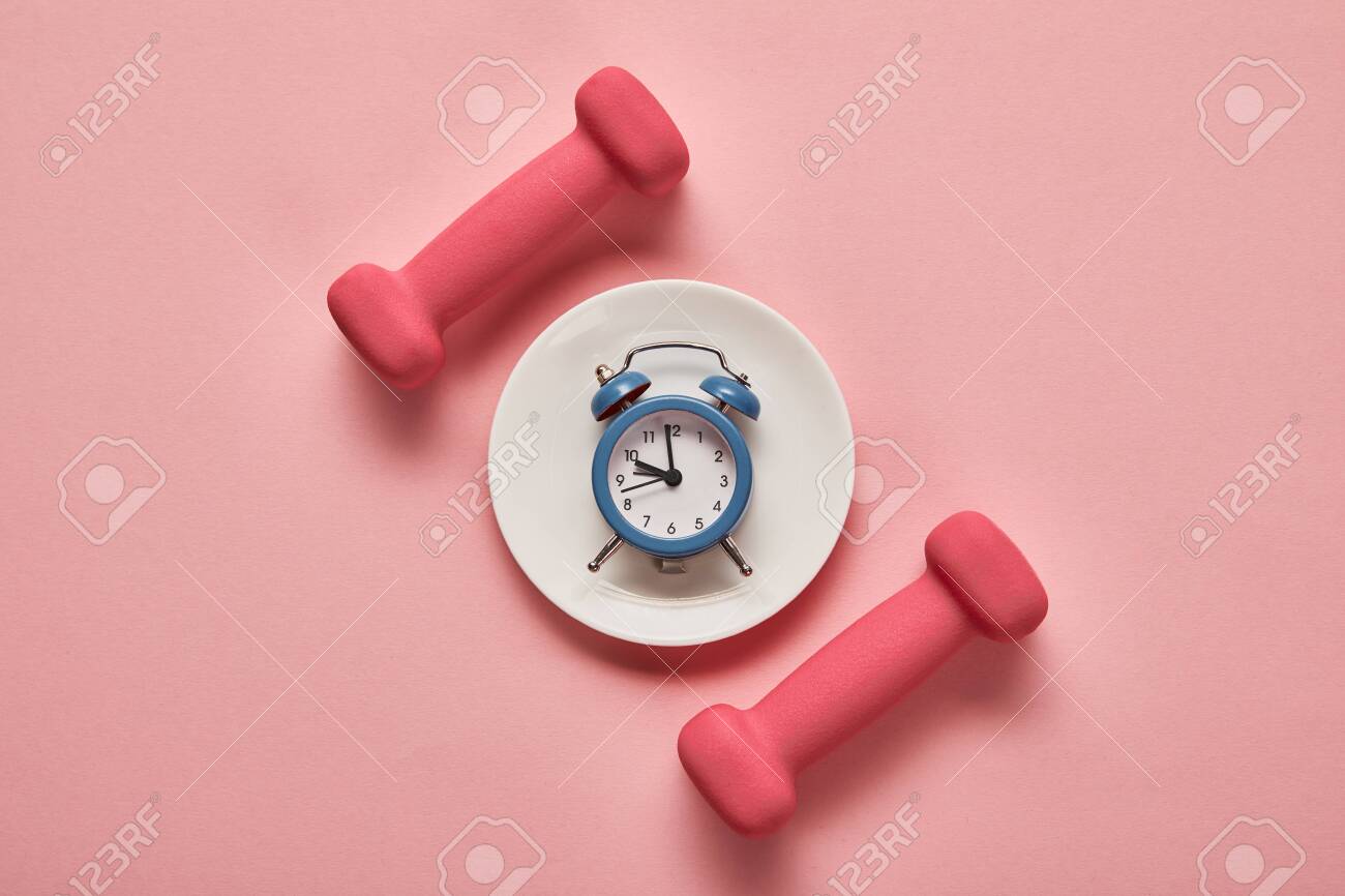 top view of dumbbells and plate with toy alarm clock on pink background - 130573554 top view of dumbbells and plate with toy alarm clock on pink background - 130573554