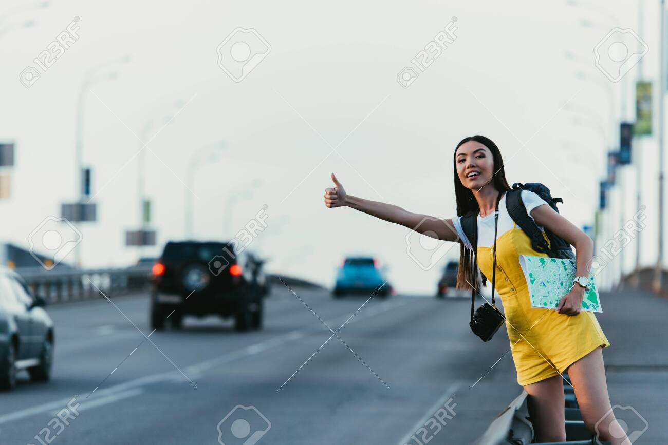 beautiful and asian woman in yellow overalls hitchhiking and holding map - 132354498 beautiful and asian woman in yellow overalls hitchhiking and holding map - 132354498