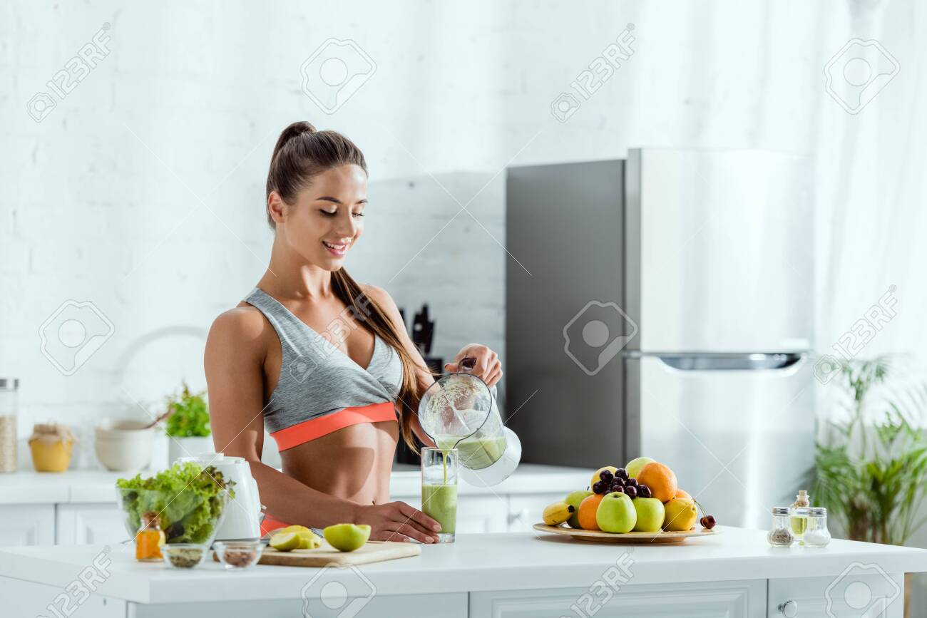 happy woman with sportswear pouring smoothie in glass near fruits - 131260419 happy woman with sportswear pouring smoothie in glass near fruits - 131260419