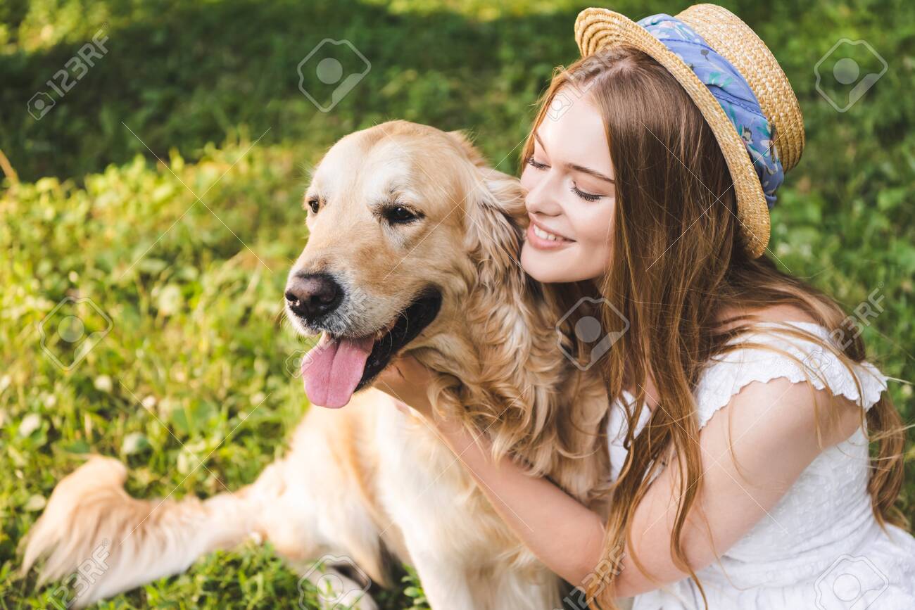 beautiful girl in white dress and straw hat hugging golden retriever while sitting on meadow and looking at dog - 131261680 beautiful girl in white dress and straw hat hugging golden retriever while sitting on meadow and looking at dog - 131261680