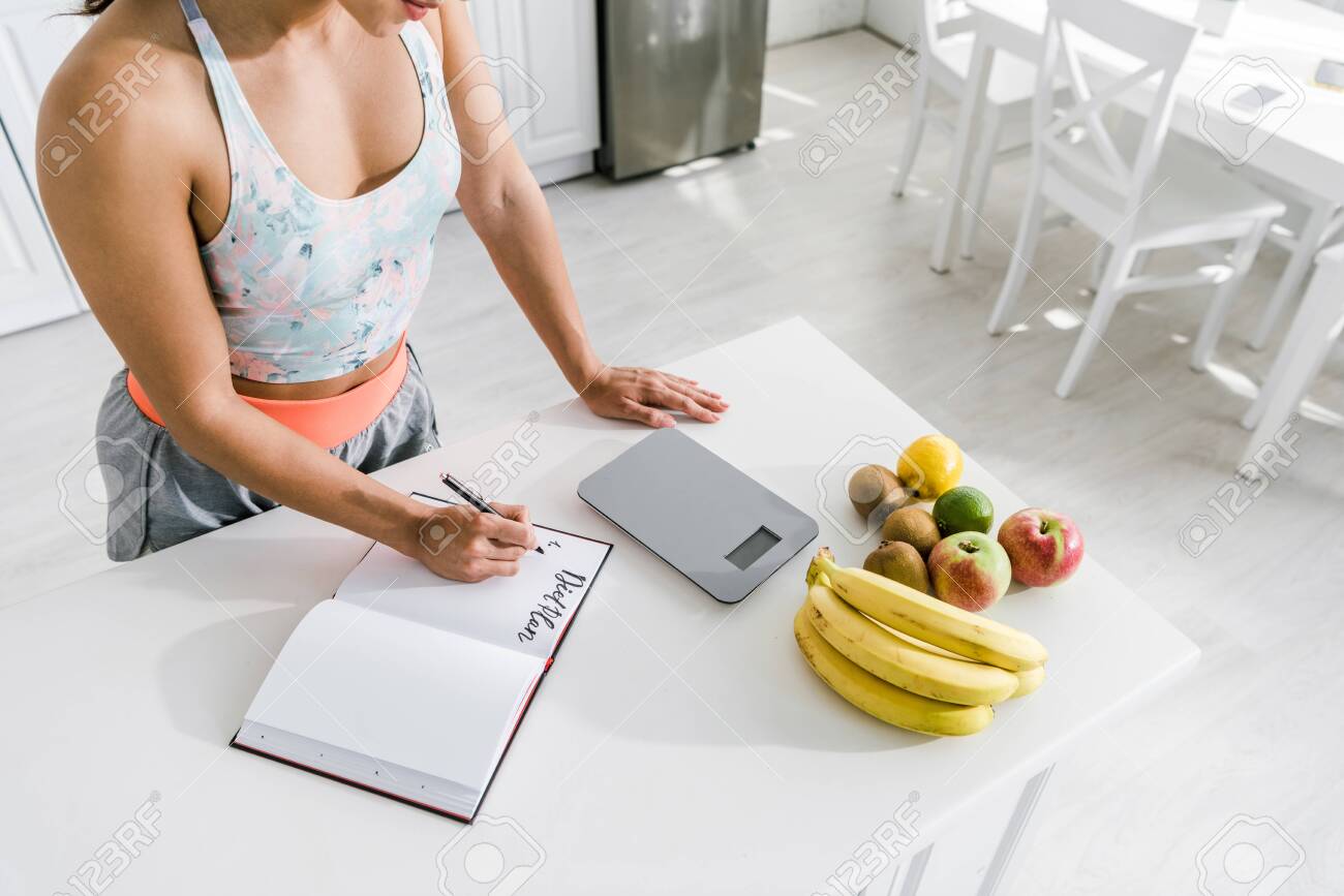 cropped view of woman holding pen near notebook with lettering and fruits - 131261019 cropped view of woman holding pen near notebook with lettering and fruits - 131261019