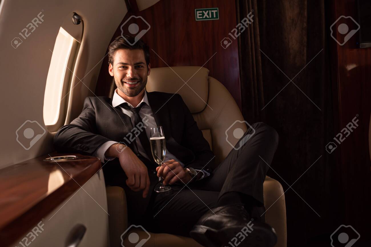handsome smiling man holding glass of champagne in plane - 132946146 handsome smiling man holding glass of champagne in plane - 132946146
