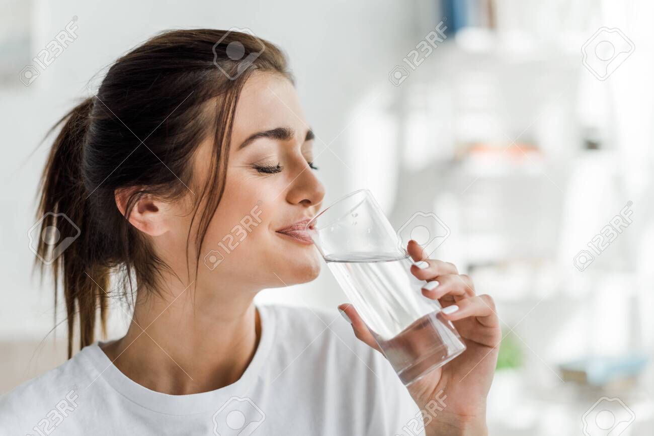 smiling girl holding drinking water from glass in the morning - 134003917 smiling girl holding drinking water from glass in the morning - 134003917