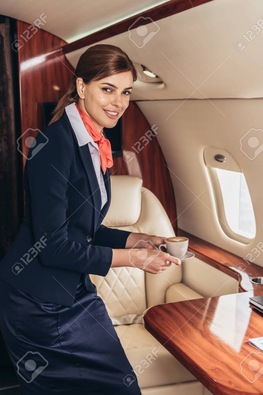Smiling Flight Attendant In Uniform Looking At Camera And Holding Cup In Private Plane Stock Photo, Picture And Royalty Free Image. Image 134051772.