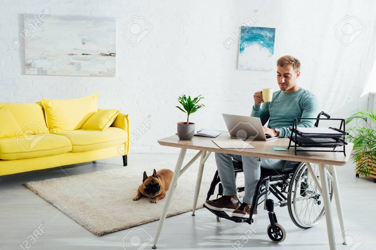 Disabled man with laptop and cup and french bulldog in living room - 134076070 Disabled man with laptop and cup and french bulldog in living room - 134076070