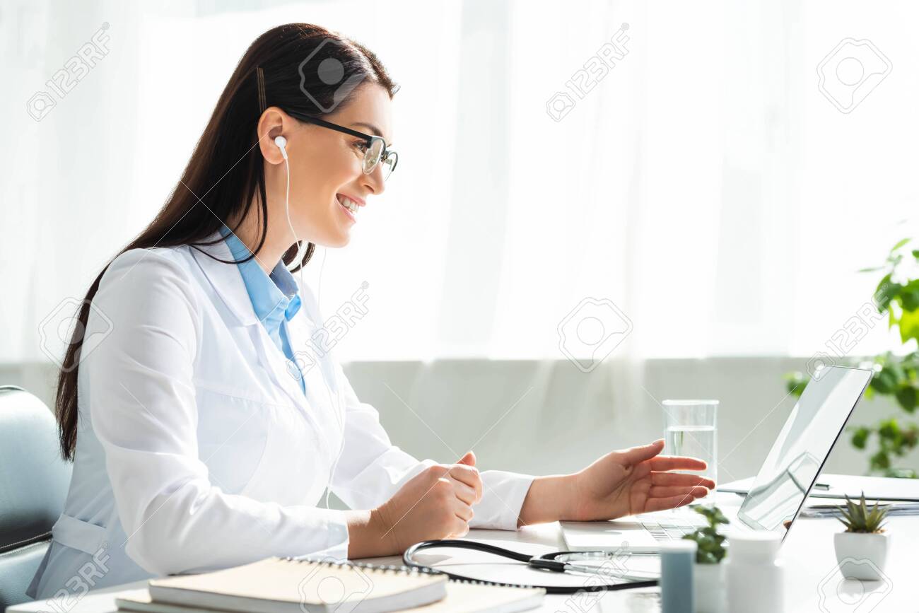 positive doctor in earphones having online consultation with patient on laptop in clinic office - 134984775 positive doctor in earphones having online consultation with patient on laptop in clinic office - 134984775