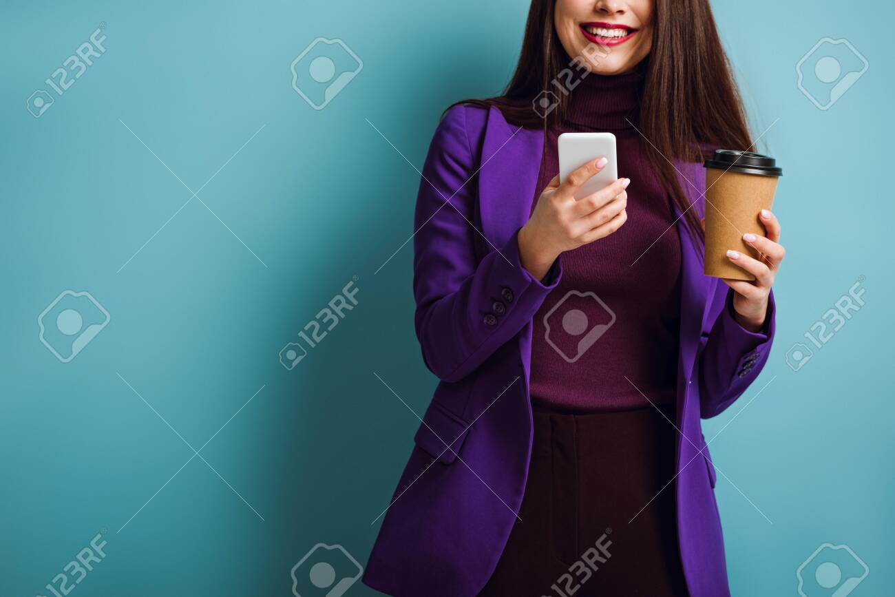 cropped view of smiling girl chatting on smartphone while holding coffee to go on blue background - 141041408 cropped view of smiling girl chatting on smartphone while holding coffee to go on blue background - 141041408