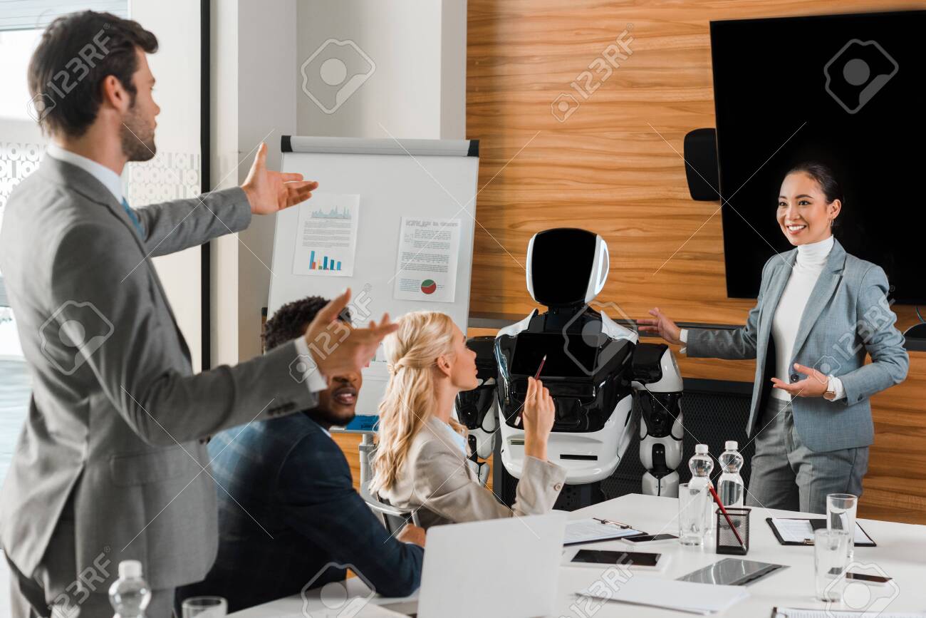 attractive asian businesswoman pointing with hands at robot near colleagues in conference hall - 141256779 attractive asian businesswoman pointing with hands at robot near colleagues in conference hall - 141256779