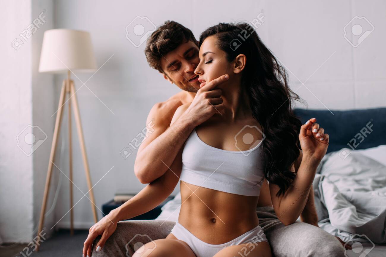 Man Smiling, Touching Female Face And Sitting Near Girl With Closed Eyes On  Bed In Bedroom Stock Photo, Picture and Royalty Free Image. Image 145945699.