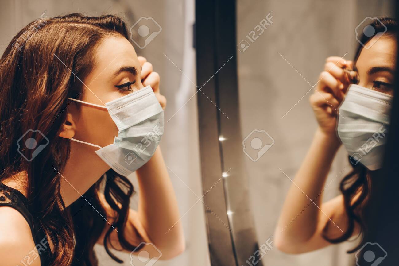selective focus of attractive woman in medical mask applying eye shadow in bathroom - 147994495 selective focus of attractive woman in medical mask applying eye shadow in bathroom - 147994495
