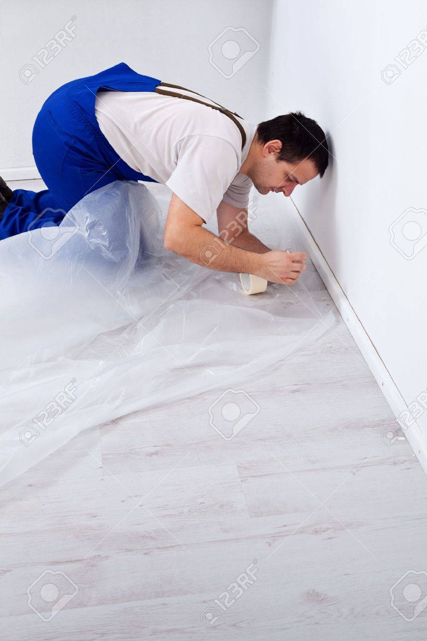 Worker Laying Protection Film Before Painting Kneeling On The
