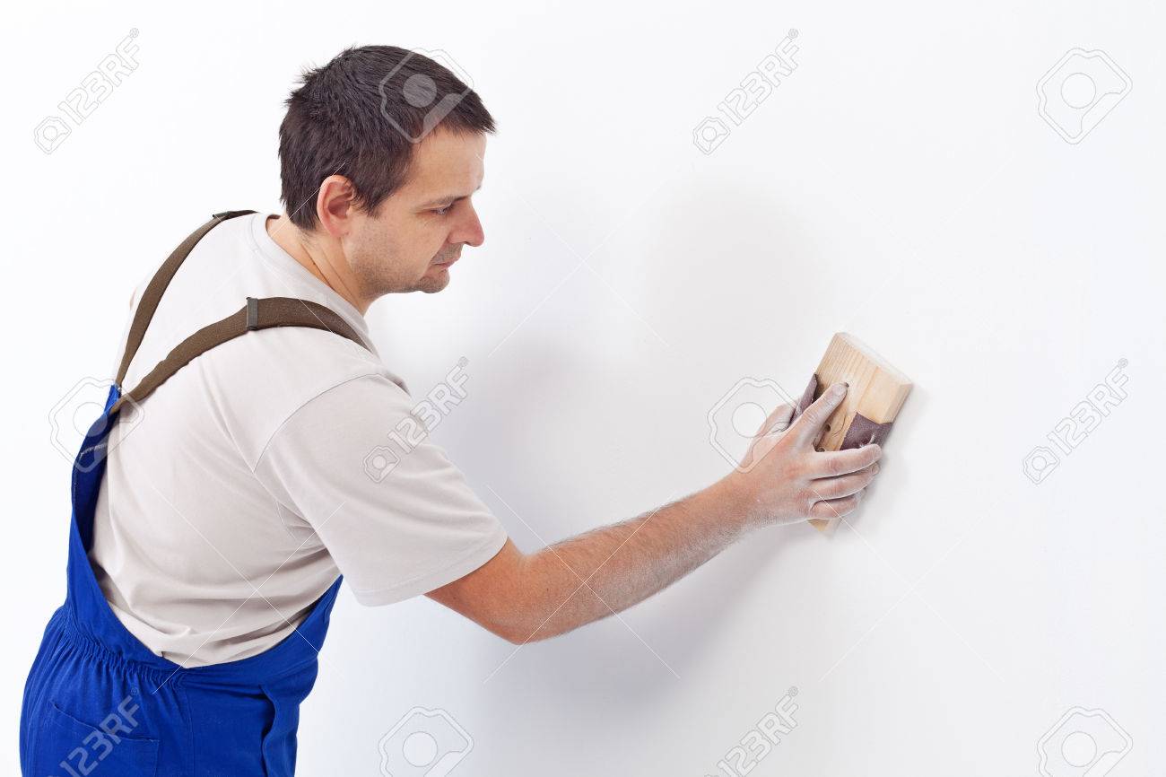 Worker scrubbing the wall with sandpaper - preparing the surface for painting - 22247598 Worker scrubbing the wall with sandpaper - preparing the surface for painting - 22247598