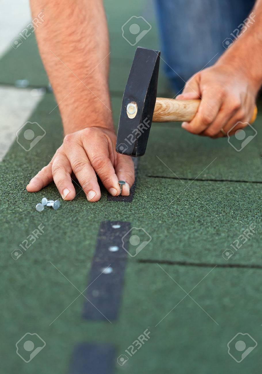 Worker installs bitumen roof shingles - closeup on hands with nails and hammer - 25754272 Worker installs bitumen roof shingles - closeup on hands with nails and hammer - 25754272