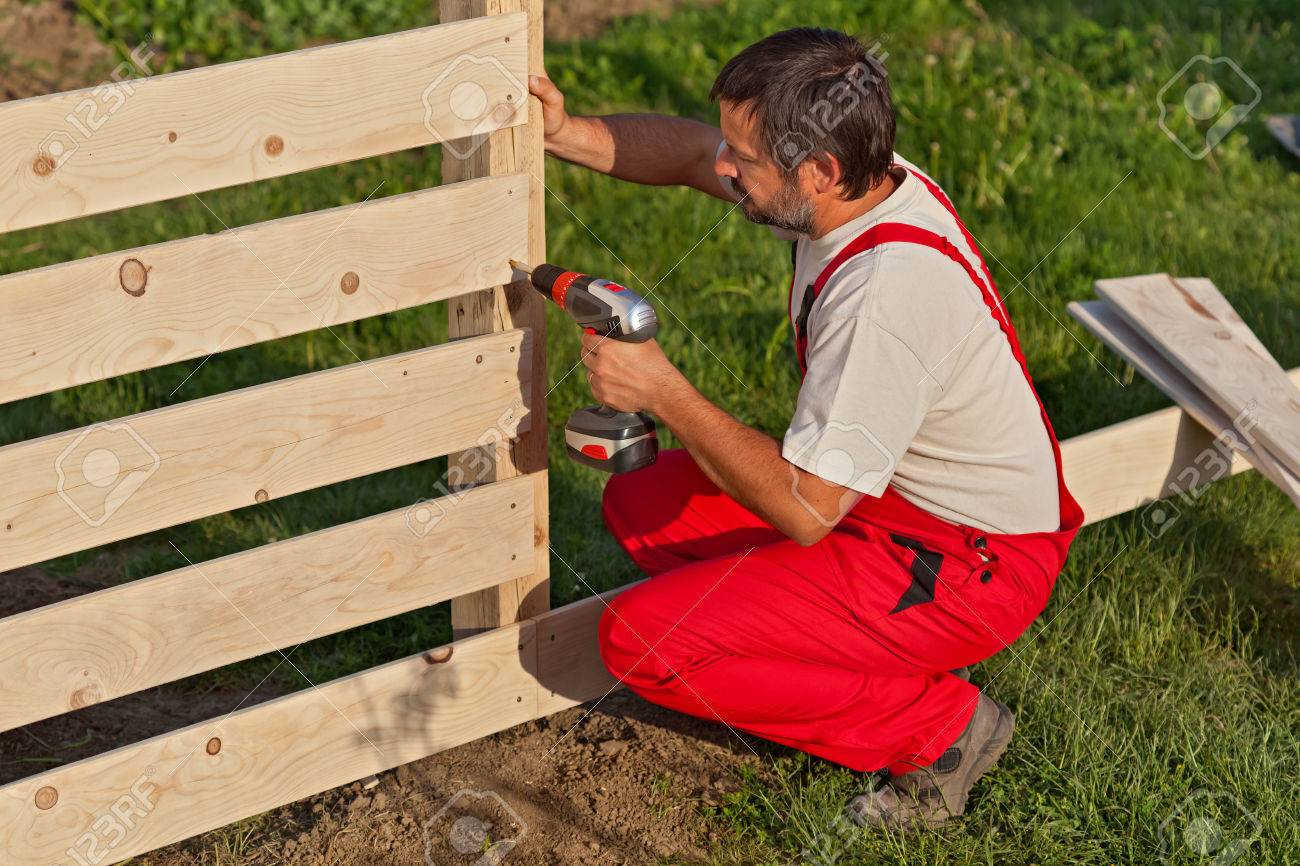 Man building a wooden fence - fastening the boards with screws - 55262324 Man building a wooden fence - fastening the boards with screws - 55262324