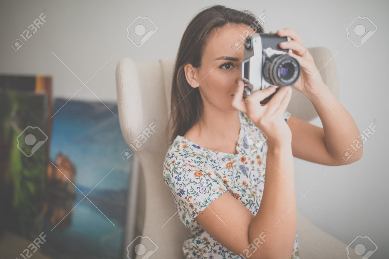 Pretty, young female photographer in her studio taking photos with a vintage film camera (color toned image) - 169294148 Pretty, young female photographer in her studio taking photos with a vintage film camera (color toned image) - 169294148