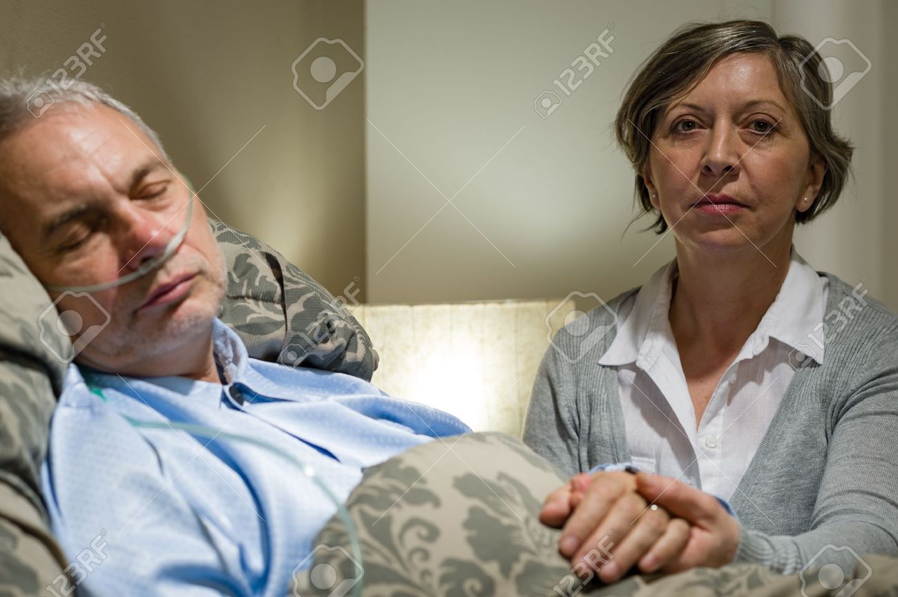 思いやりのある妻のベッドに横たわってシニアは病気の主人の手を繋いでいます の写真素材 画像素材 Image