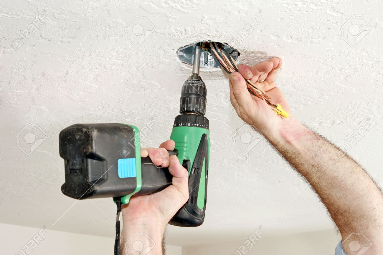 An Electrician S Hands Using A Drill To Screw A Fan Box Into