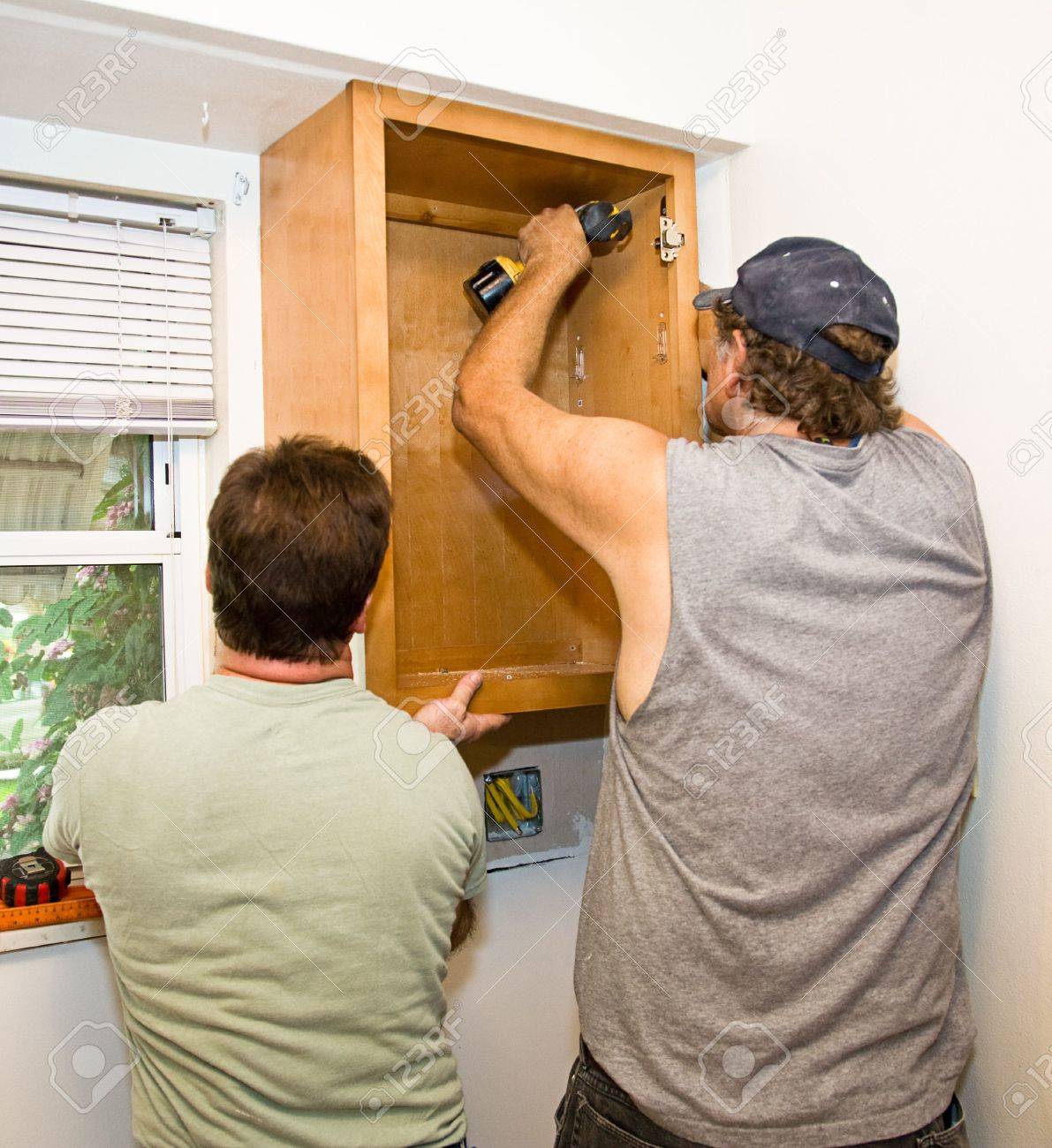 Carpenter And Helper Installing Kitchen Cabinets Together Stock