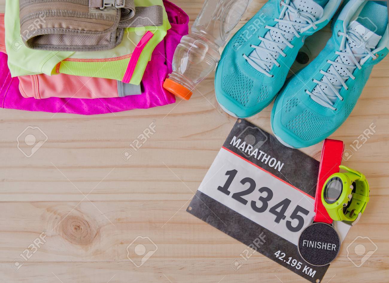 Vista Superior Del Traje Para El Corredor En El Fondo De Madera: Número De Dorsal, Medalla De Finisher, El Reloj Gps, Zapatillas Deportivas, Pantalones Cortos, Camisa Y El Sujetador Del Deporte.
