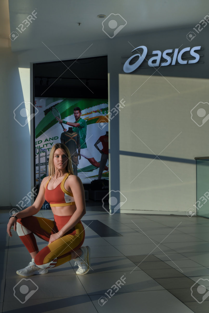 Skopje, Northern Macedonia - March 12, 2021: Asics store in Skopje, Northern Macedonia. Girl photo model wearing sports tracksuits and sneakers ASICS GEL, kneeling posing in front of a sports shop - 166164681 Skopje, Northern Macedonia - March 12, 2021: Asics store in Skopje, Northern Macedonia. Girl photo model wearing sports tracksuits and sneakers ASICS GEL, kneeling posing in front of a sports shop - 166164681
